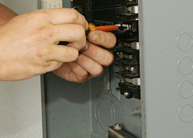 An electrician working on an electrical breaker panel. Model is an actual electrician - all work is being performed according to industry codes and safety standards.